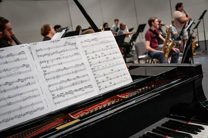 Sheet music on piano with students playing instruments in background
