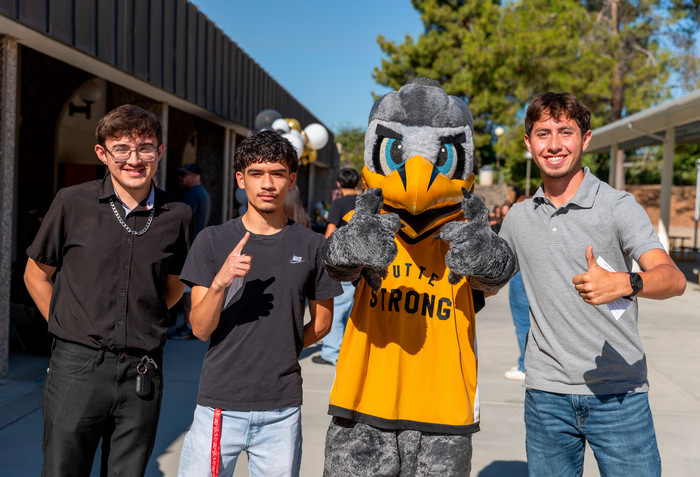 three-male-students-pose-with-dash-mascot-at-campus-event