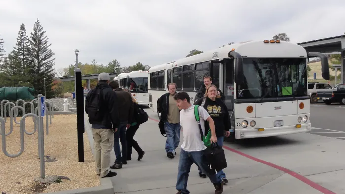 Students exit bus in campus parking lot